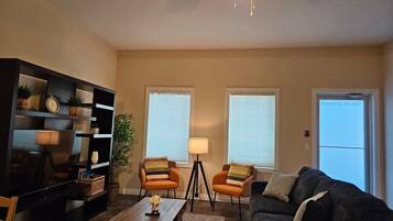 A living room with a sofa, two armchairs, a coffee table, a TV, and a bookshelf.