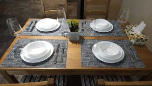 Taula de dinar posta per a quatre amb sotsplats, plats, coberts i gots.