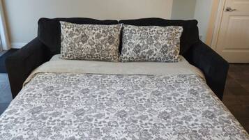 A bed with a floral-patterned bedspread, two matching pillows, and a painting of trees on the wall.