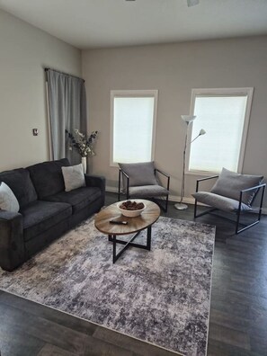 Ein modernes Wohnzimmer mit einem dunkelgrauen Sofa, zwei Sesseln, einem Couchtisch und einer Stehlampe.