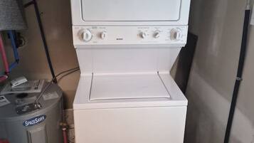 A compact laundry room with a white washer and dryer, a water heater, and a storage tank.