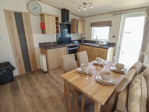 A compact kitchen with wooden cabinets, a stove, and a dining area set for four with a table and chairs. - Tattershall Lakes Country Park - Holiday Accommodation 16408 (Lincoln)