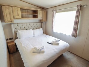 A bedroom with a bed, a headboard, a nightstand, a wardrobe, and a window with curtains. - Tattershall Lakes Country Park - Holiday Accommodation 16408 (Lincoln)