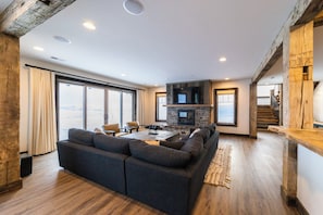 A modern living room with a sectional sofa, a fireplace, and a view through large windows.