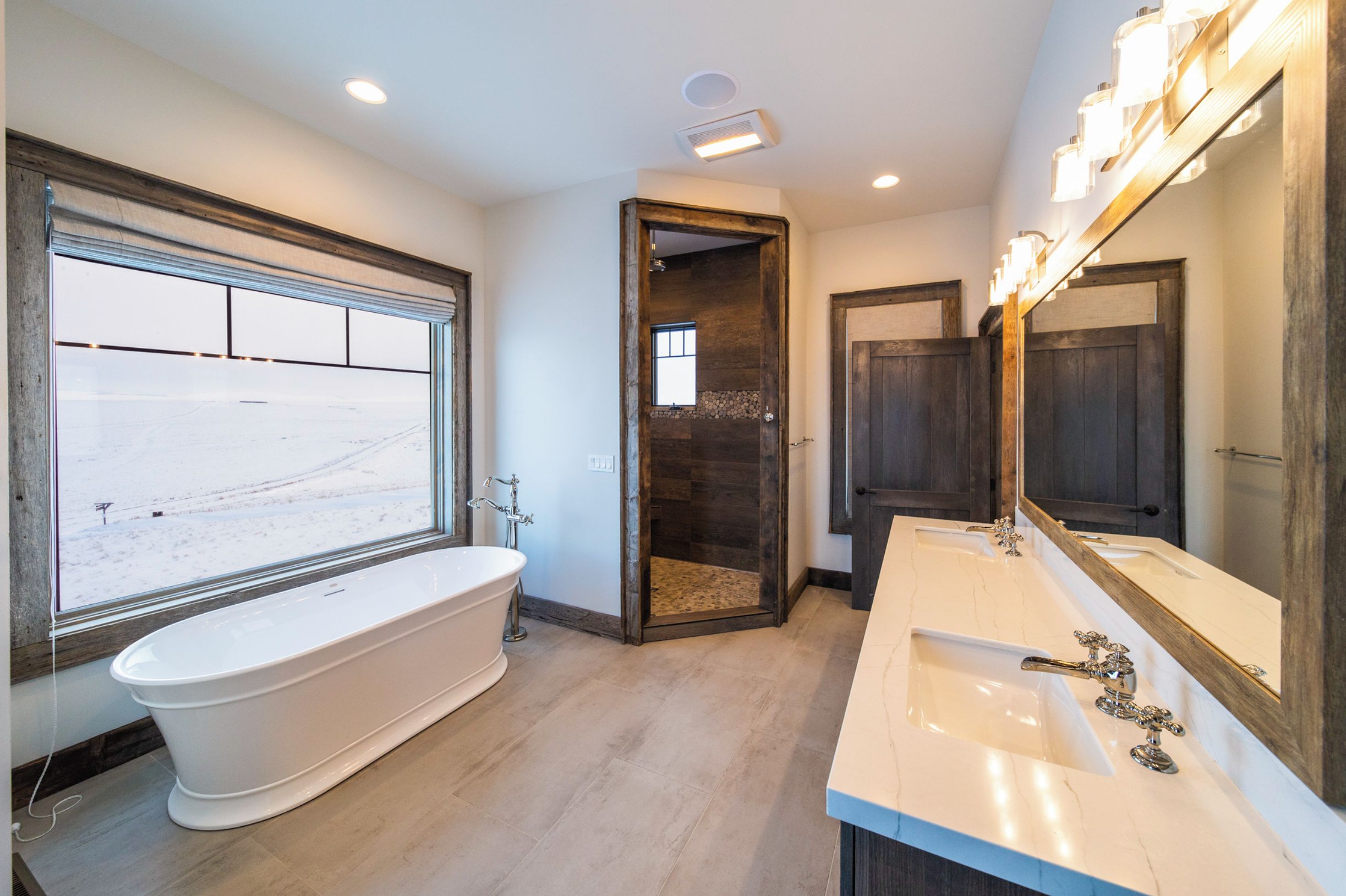 A bathroom with a freestanding bathtub, a large mirror, and a window with a view of a snowy landscape.