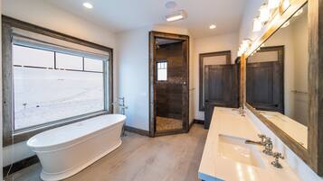 A bathroom with a freestanding bathtub, a large mirror, and a window with a view of a snowy landscape.