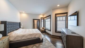 A bedroom with a bed, dresser, chair, and large windows.
