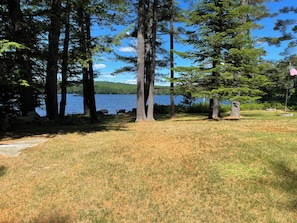 A lakeside campsite with a clear view of the water, surrounded by tall trees and a grassy area. - Charming 3-bedroom cabin on David Pond (Fayette)
