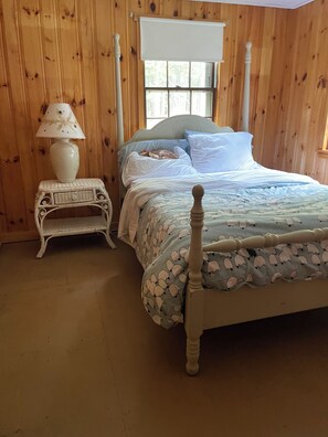 A wooden-paneled room with a bed, a nightstand, and a window with a white blind. - Charming 3-bedroom cabin on David Pond (Fayette)