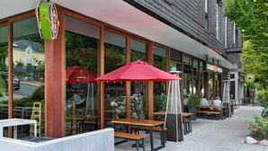 Een terras met tafels en parasols, een gebouw van baksteen met grote ramen, en een bord voor een pizzeria.