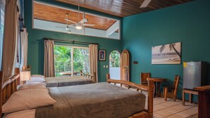 A room with a bed, a desk, a chair, a ceiling fan, and a view of greenery outside. - Rick's Place (Guiones)