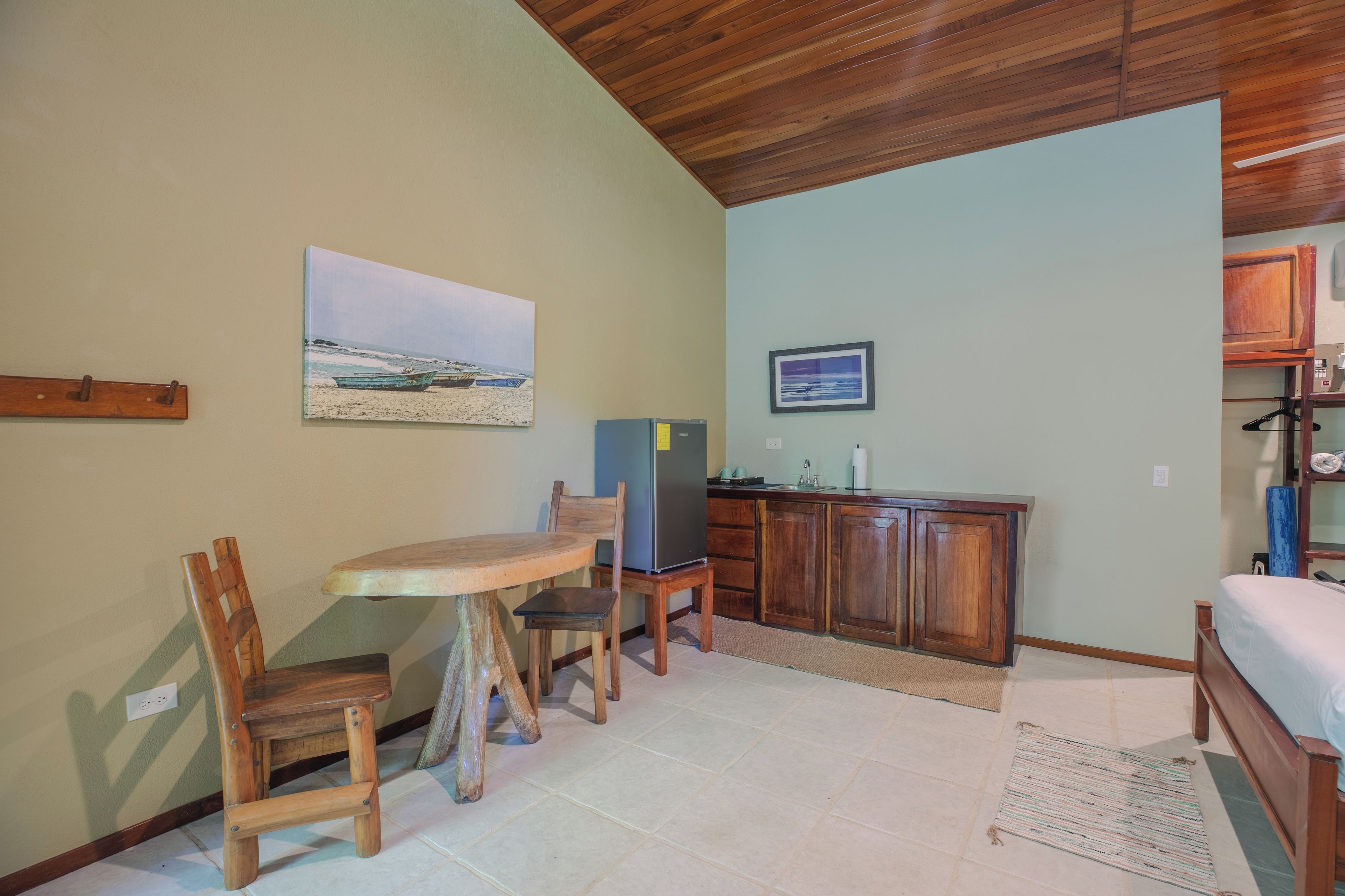 Una habitación compacta con una mesa de madera, sillas, una pequeña kitchenette y una cama.