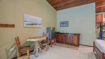 Una habitación compacta con una mesa de madera, sillas, una pequeña kitchenette y una cama.