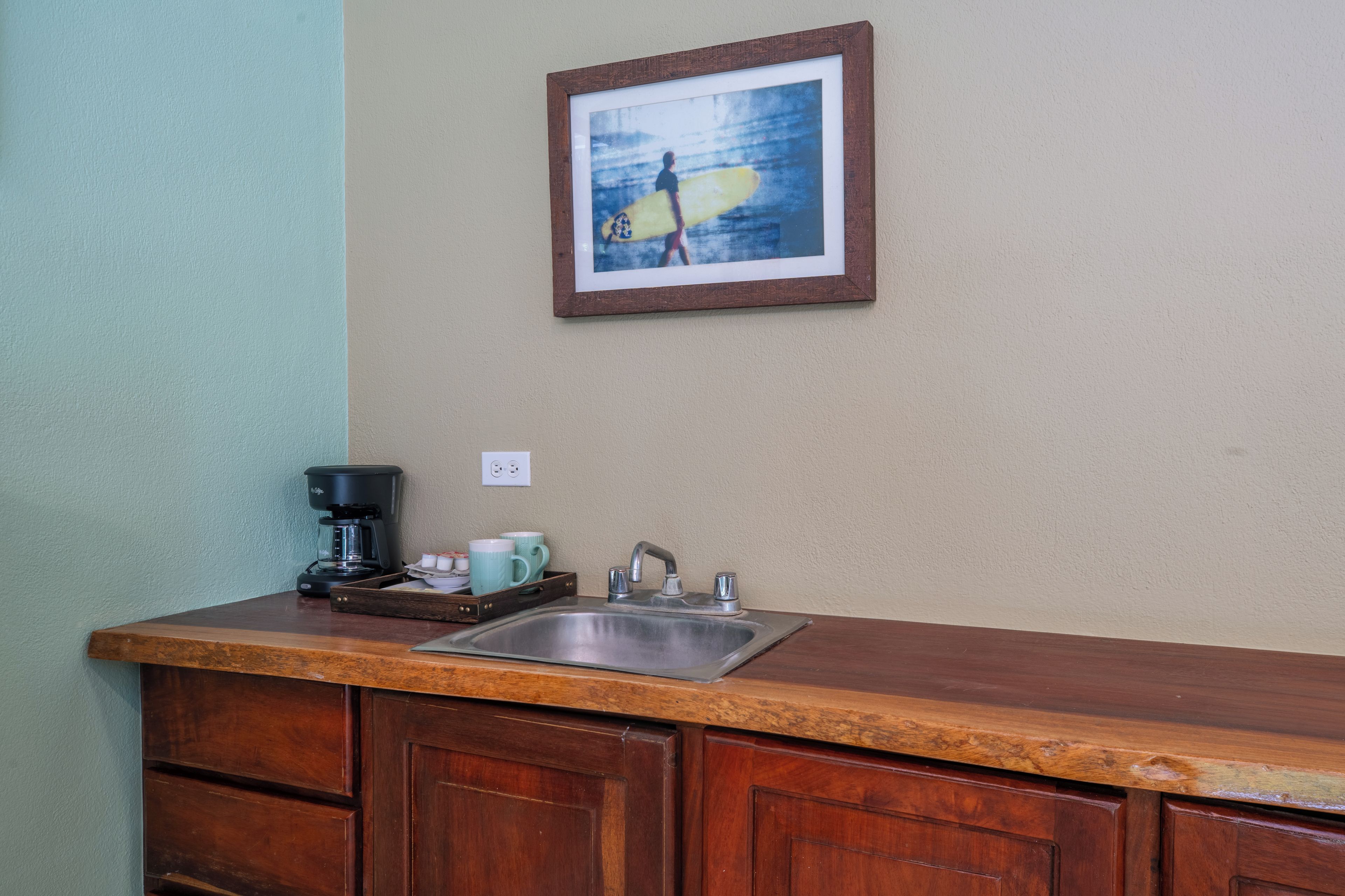 Una cocina con encimera de madera, cafetera, lavabo y un cuadro en la pared.