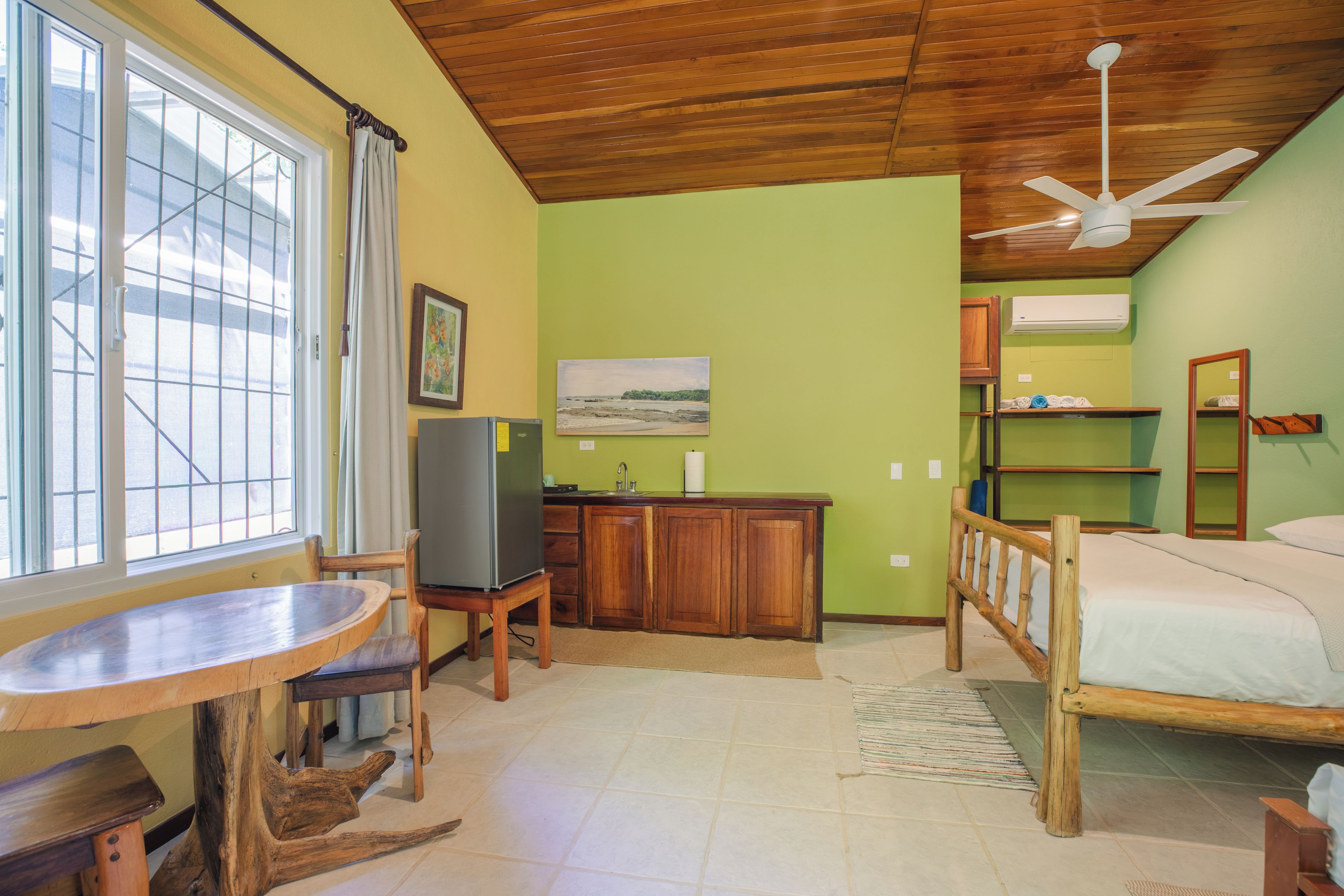 Habitació compacta amb llit, taula de menjador, zona de cuina i finestra amb cortines.