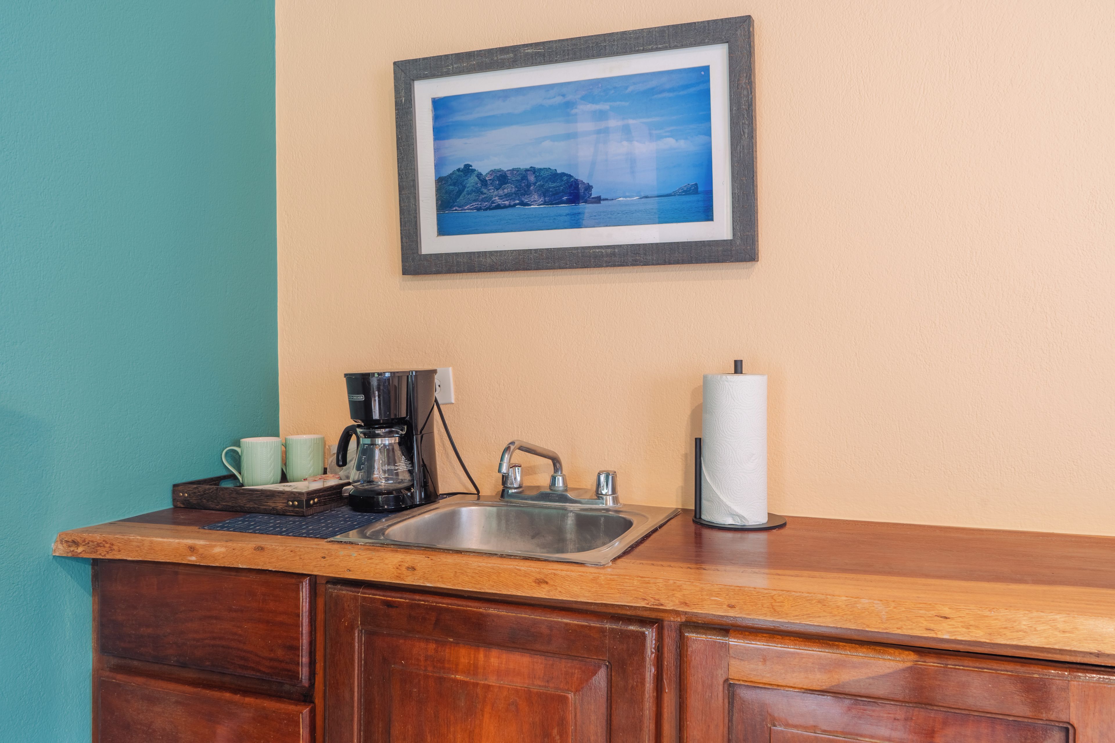 A kitchen with a wooden countertop, a coffee maker, a sink, and a framed picture on the wall.