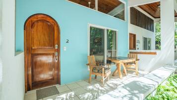 Puerta de madera con el número '2' en la pared, una mesa de madera con sillas y vistas a la vegetación.
