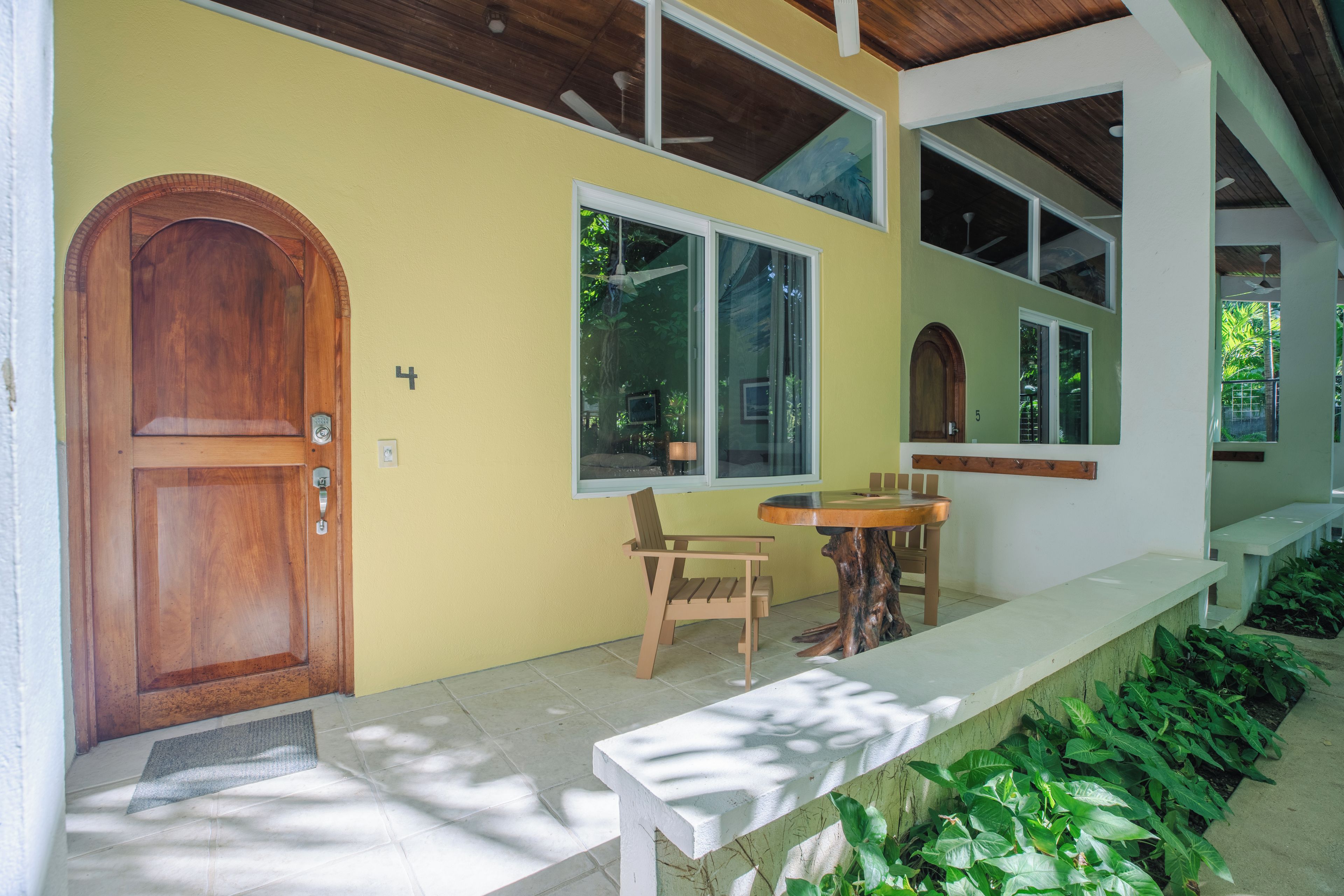 Una puerta de madera con una placa de número, un banco, una mesa y una ventana con vistas a zonas verdes.