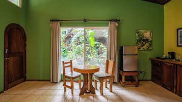 Una habitación con puerta de madera, una mesa con sillas, un refrigerador y una ventana con cortinas.