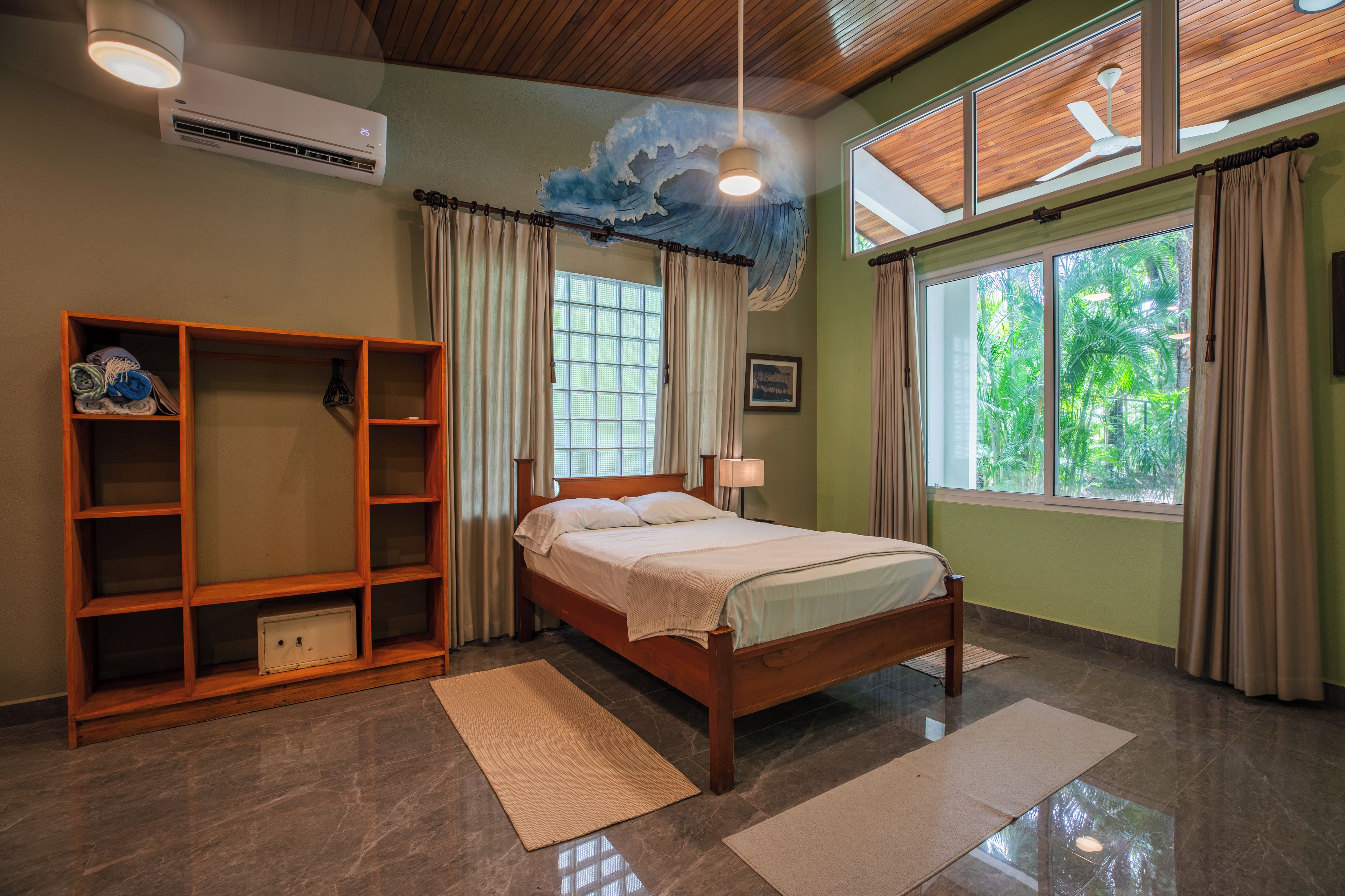 A bedroom with a bed, a wardrobe, a window with curtains, a ceiling fan, and a wall-mounted air conditioner.