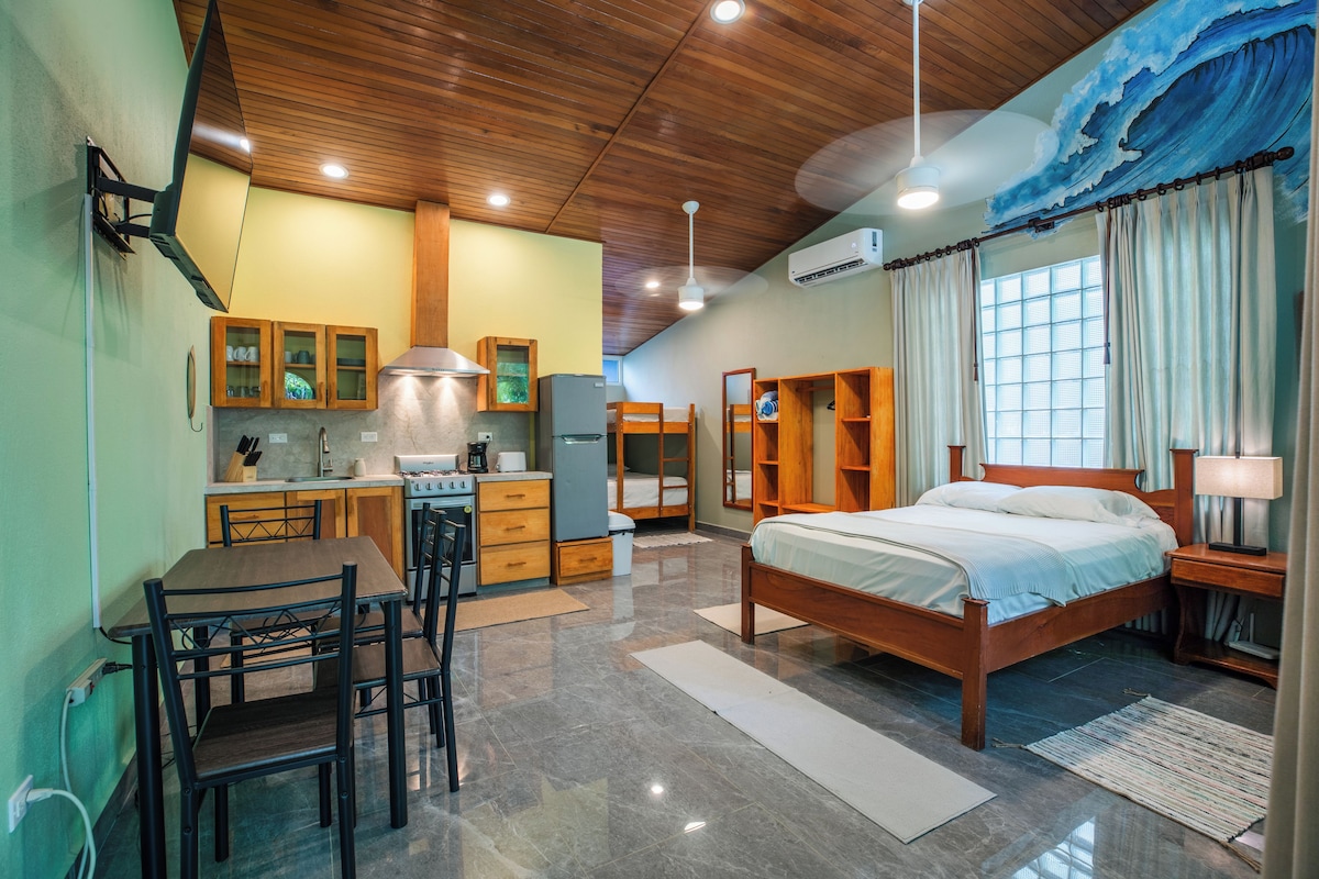 Een kleine hotelkamer met een kitchenette, een bed en een eethoek.