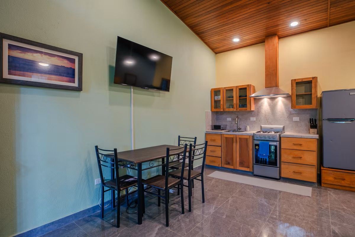 Una cocina moderna con una mesa de comedor y sillas, armarios de madera, una estufa y un televisor montado en la pared.