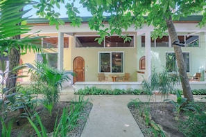 A two-story house with a front porch, a wooden door, and a window with a view of the interior. - Rick's Place (Nosara)