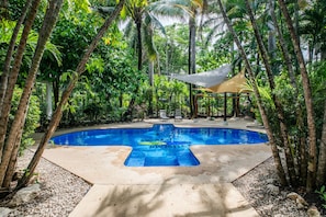 A swimming pool surrounded by tropical vegetation and a shaded seating area. - Rick's Place (Nosara)