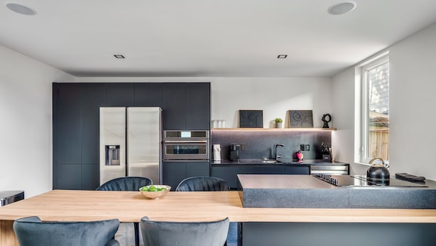 Une cuisine moderne dotée d’un îlot central, de meubles de rangement aux couleurs sombres et d’un coin repas avec des chaises.