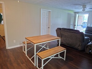 Een kamer met een houten tafel en bankje, een grijze bank en een witte deur.