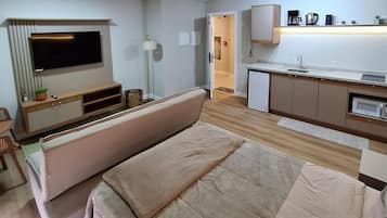Un espacio habitable compacto con sofá, televisión montada en la pared, kitchenette y pequeño comedor.