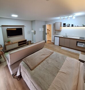 Un espacio habitable compacto con sofá, televisión montada en la pared, kitchenette y pequeño comedor.