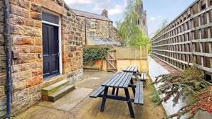 Un edificio de piedra con una puerta negra, una valla de madera y una mesa de picnic en un patio.