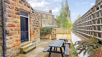 A stone building with a black door, a wooden fence, and a picnic table in a courtyard.