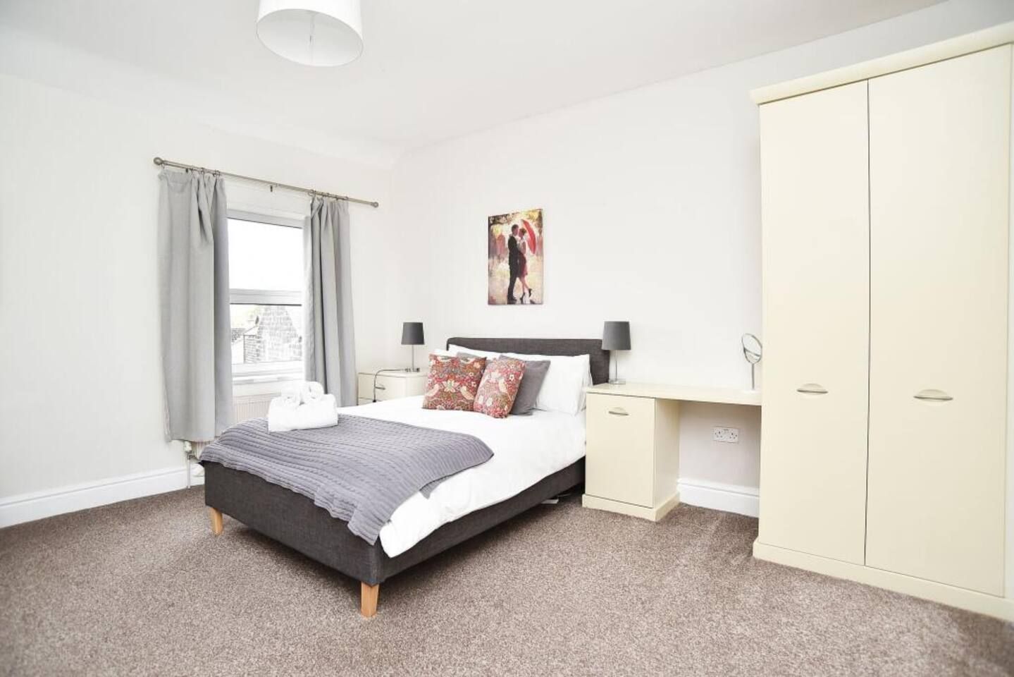 A bedroom with a bed, bedside tables, a wardrobe, and a window with curtains.