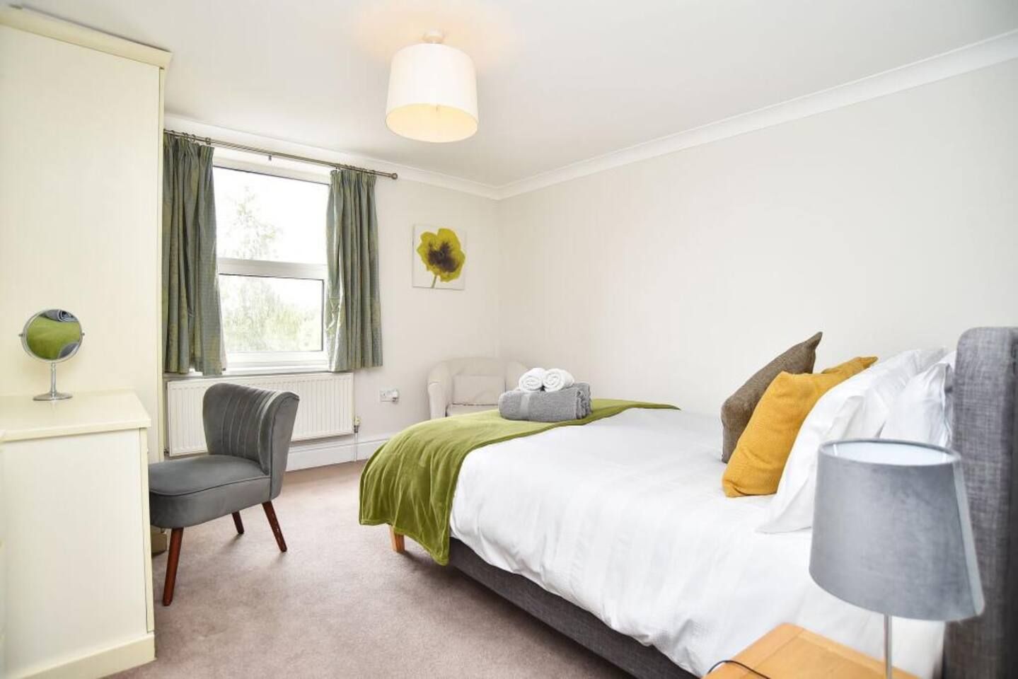 A bedroom with a bed, a chair, a lamp, a radiator, and a window with curtains.