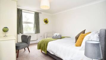 A bedroom with a bed, a chair, a lamp, a radiator, and a window with curtains.