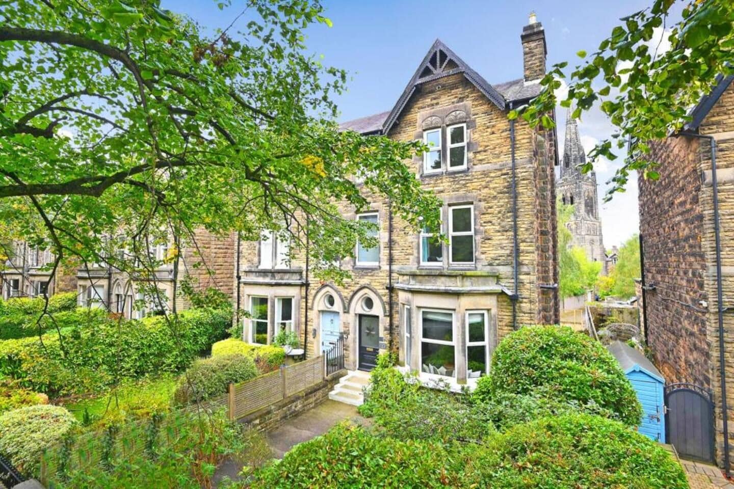 A traditional stone house with a garden, a small bridge, and a church in the background.