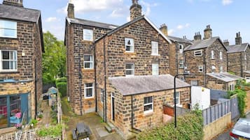A residential area with stone houses, a paved courtyard, and a car parked on the street.