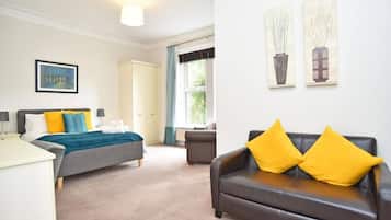 A hotel room with a bed, a sofa, a window with curtains, and artwork on the wall.