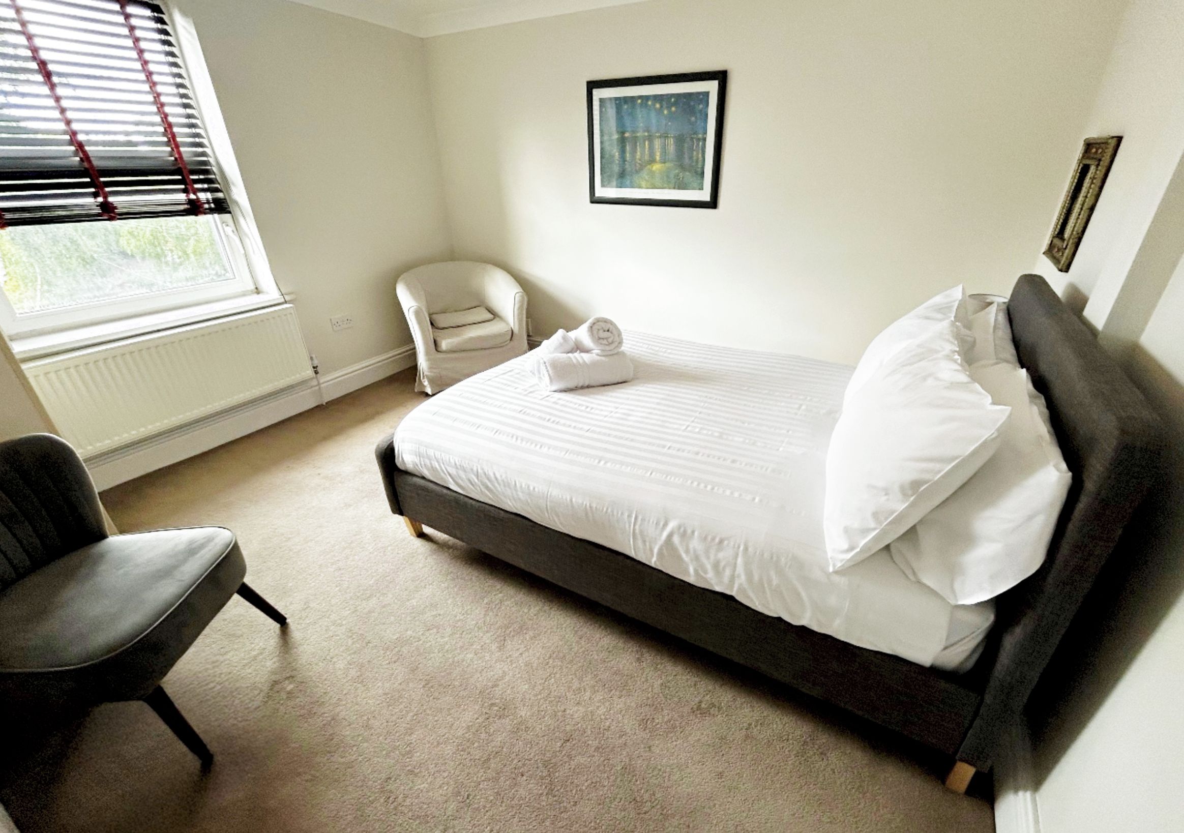 Une chambre à coucher avec un lit, une chaise, un radiateur et une fenêtre avec des stores.