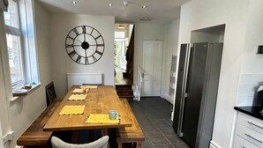 Una cocina con una mesa de madera, sillas, un reloj de pared grande y un refrigerador.