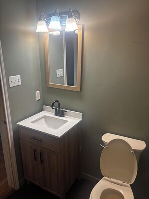 A bathroom with a white sink, dark wooden vanity, a mirror, and a toilet.