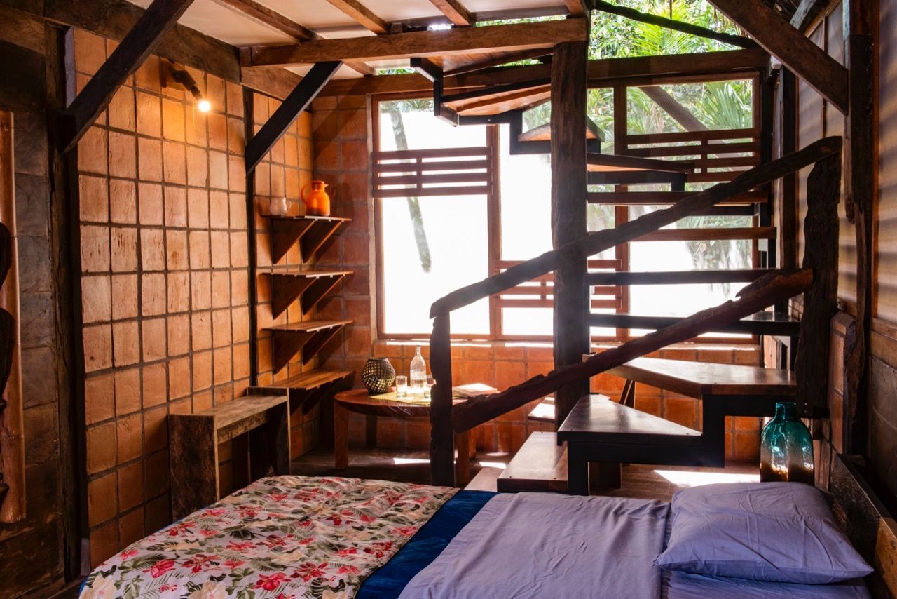 Quarto rústico com cama, prateleiras de madeira, uma mesa e escada.