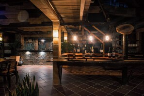 Un espace bar avec des tables et des bancs en bois, un sol carrelé et un comptoir où sont exposées des bouteilles.