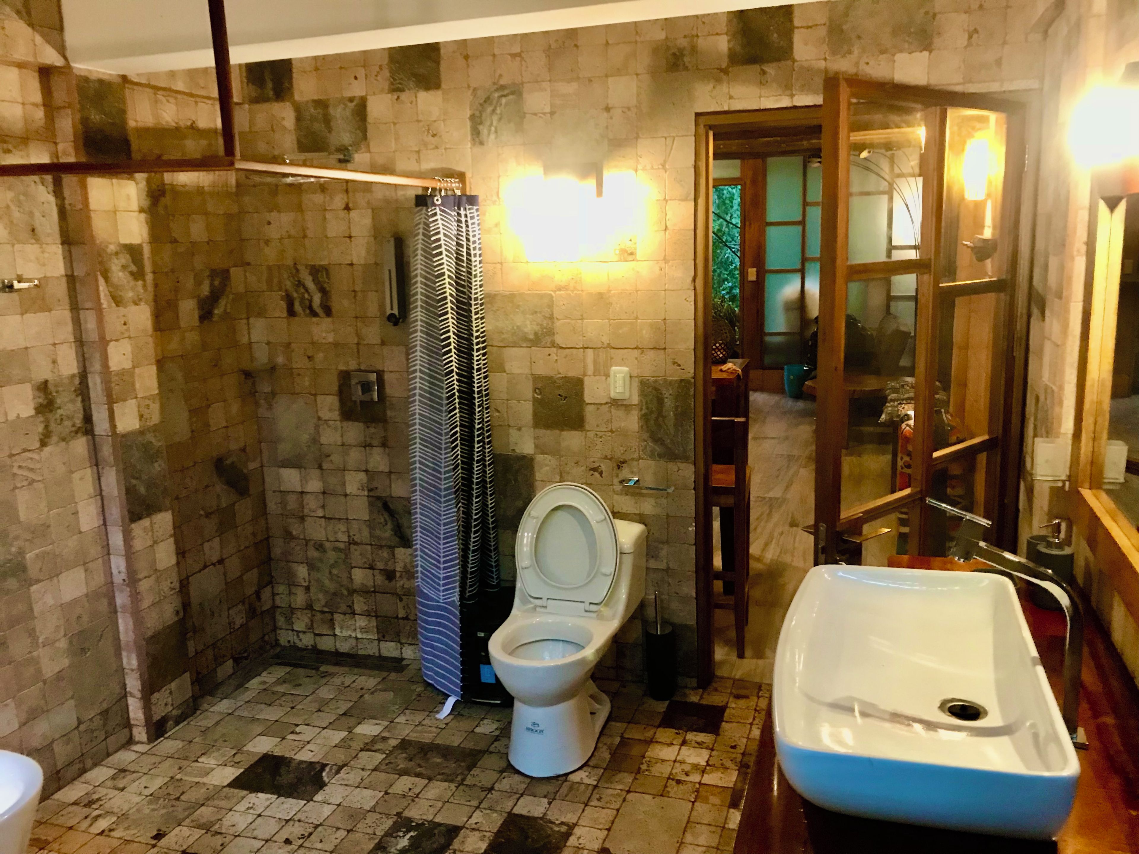 Casa de banho com chão em mosaico, sanita branca, cortina de chuveiro, lavatório e espelho.