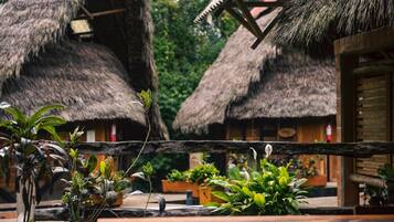 Cabanas com telhado de palha, balaústres de madeira e plantas em vasos no primeiro plano.