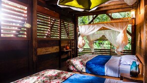 Een kamer met twee bedden, een raam met zonwering, een klamboe en houten inrichting.