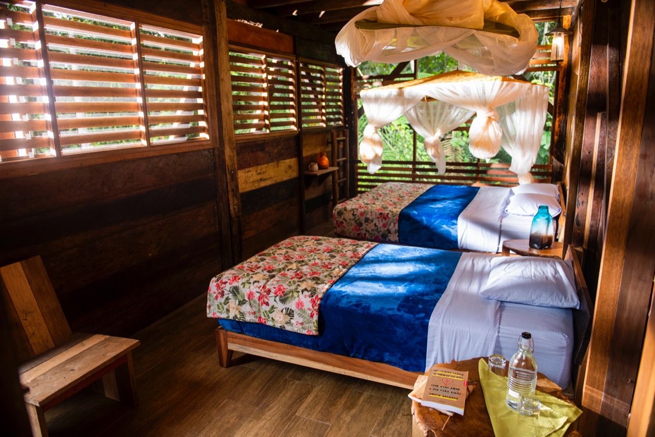 A wooden room with two beds, a bench, and a window with blinds.