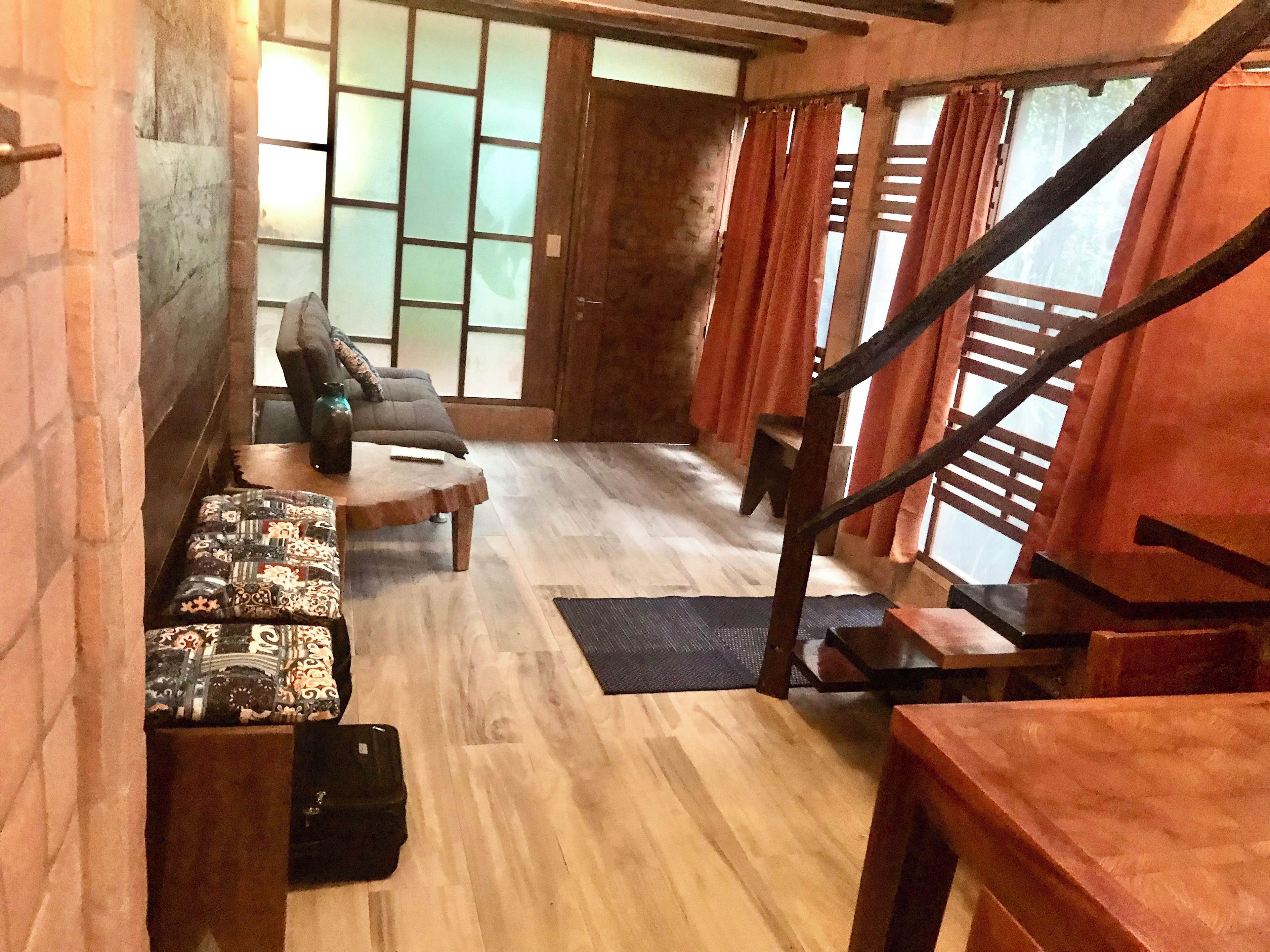 Una escalera de madera que conduce a una sala de estar con un sofá, un banco estampado y una mesita.
